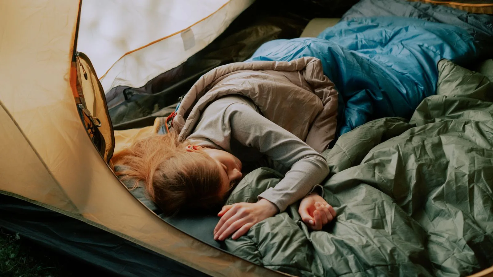 A person asleep in a sleeping bag inside a tent.