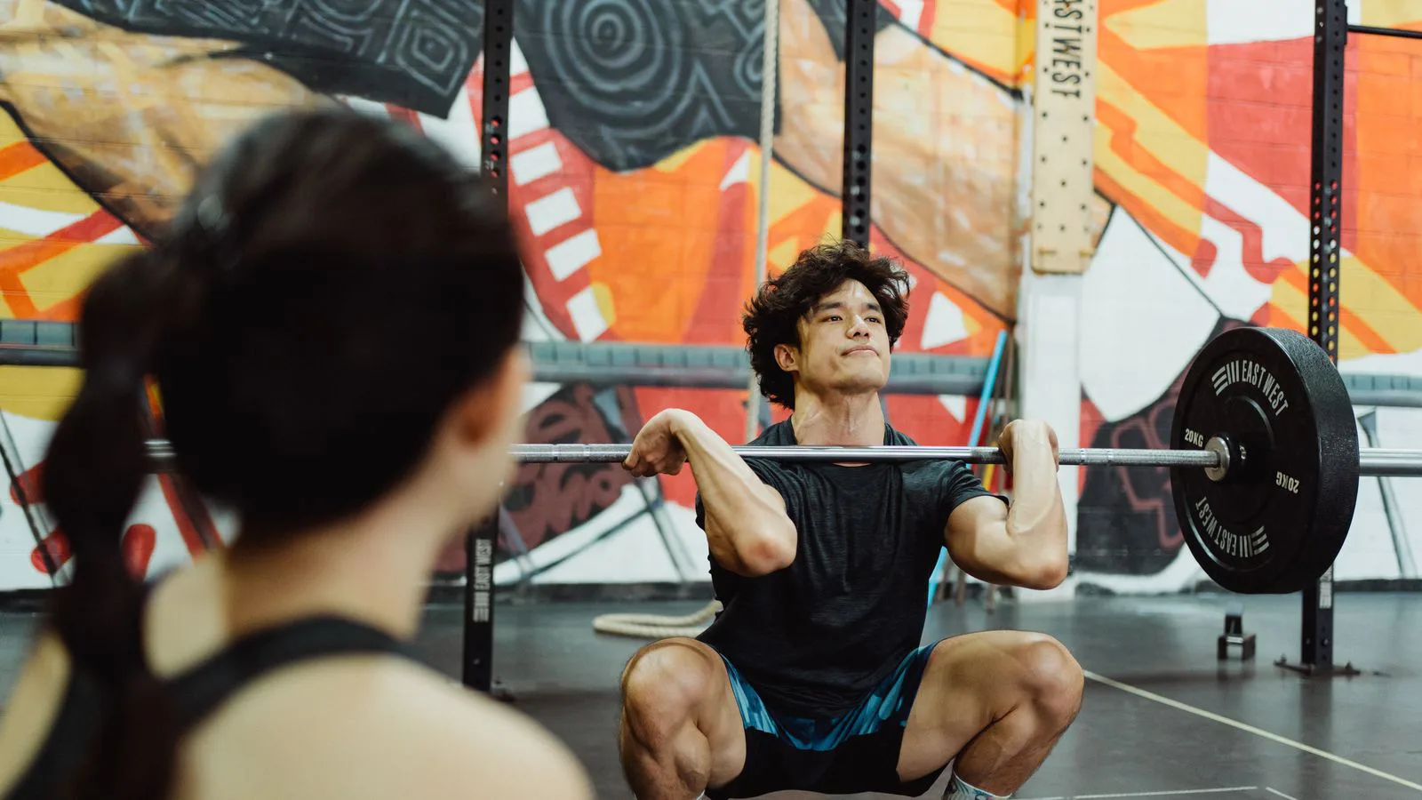 Un hombre levanta una barra en un gimnasio muy iluminado.