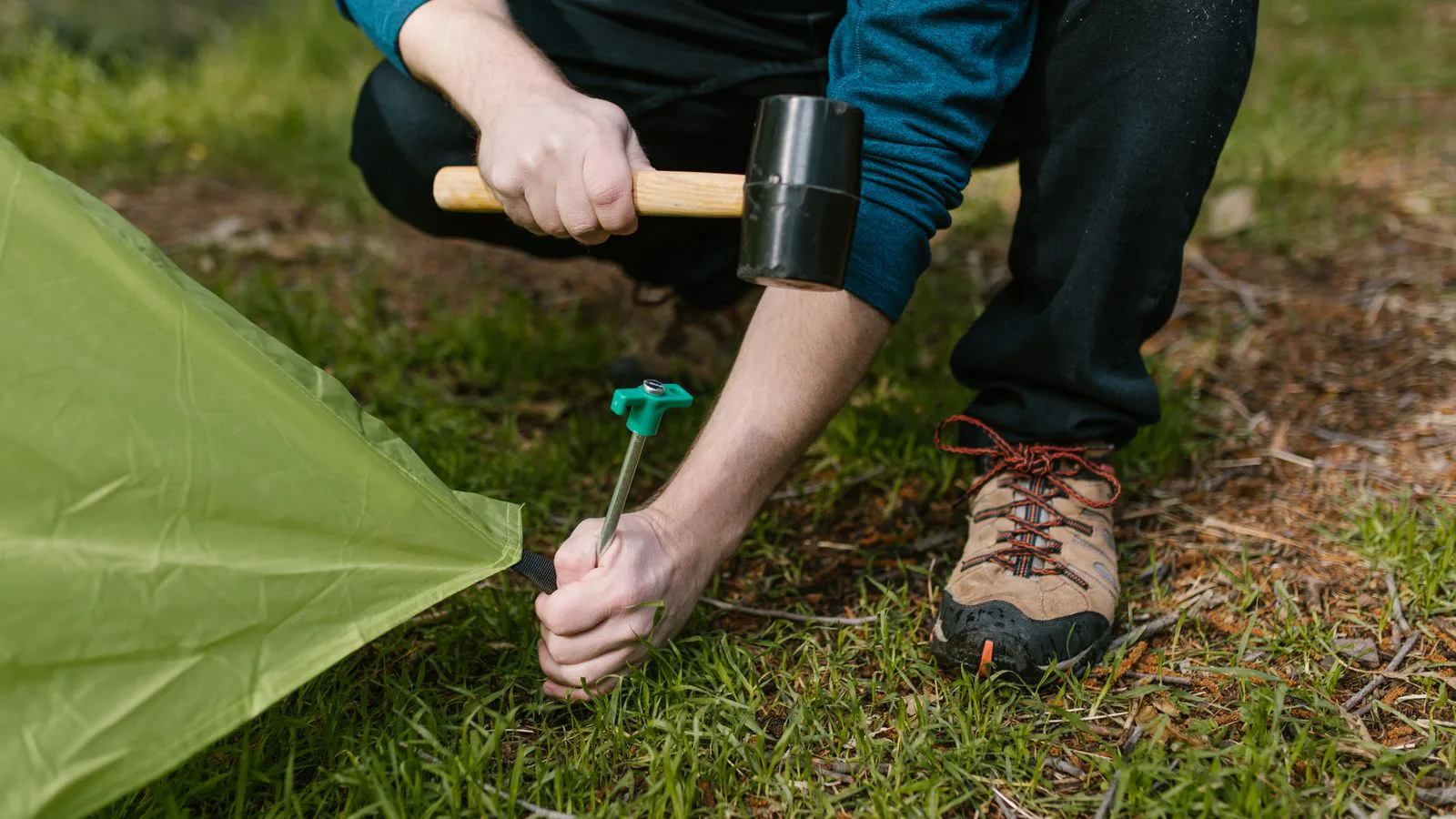 A person hammering a tent peg into the ground.