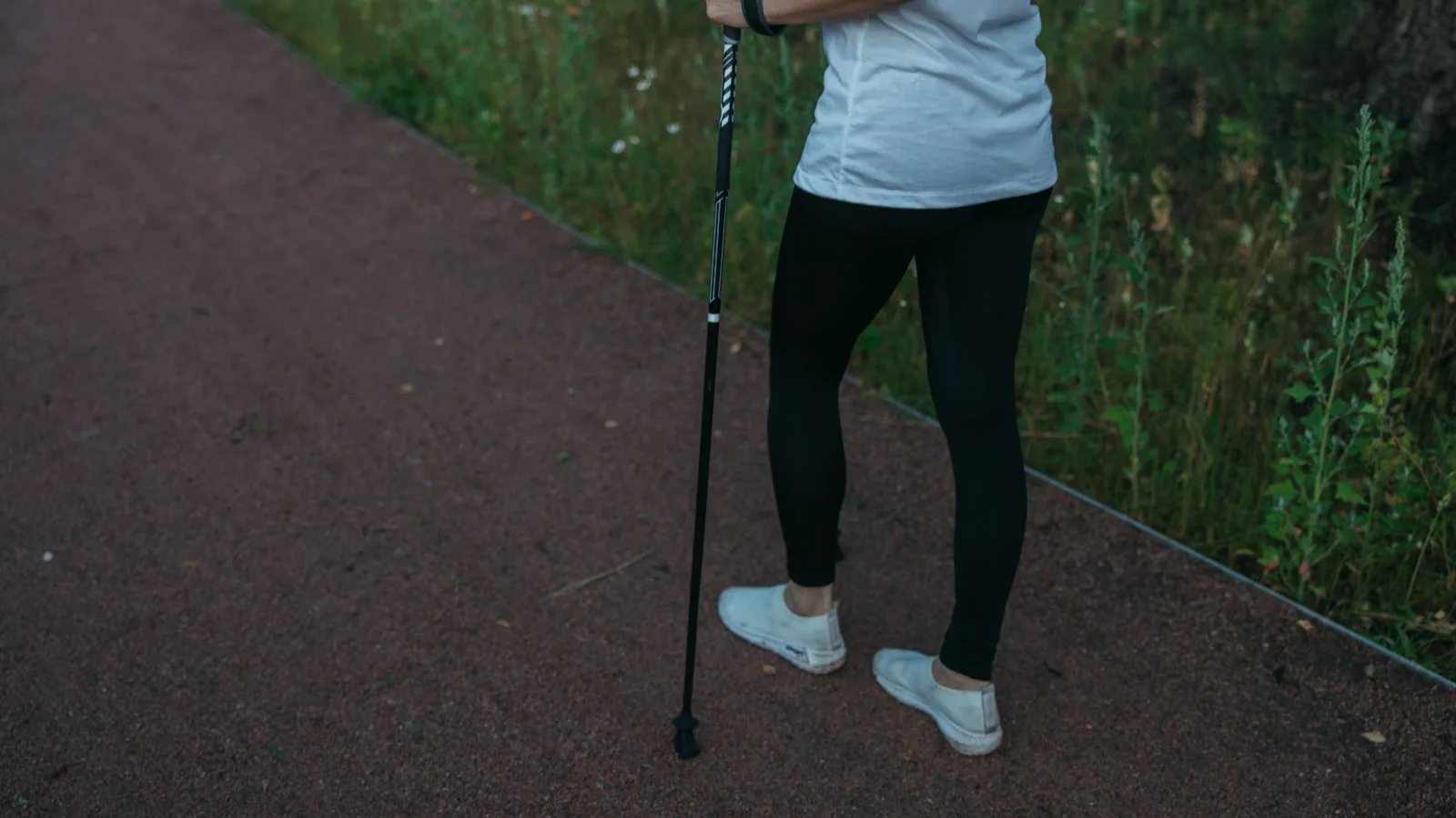 A person walking briskly on a path with a trekking pole.