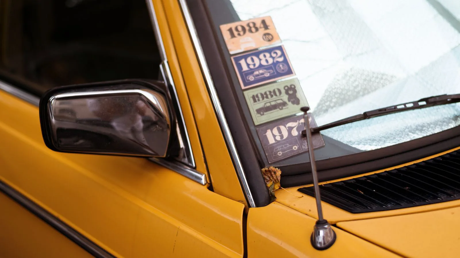 A classic yellow car with stickers across its windscreen.
