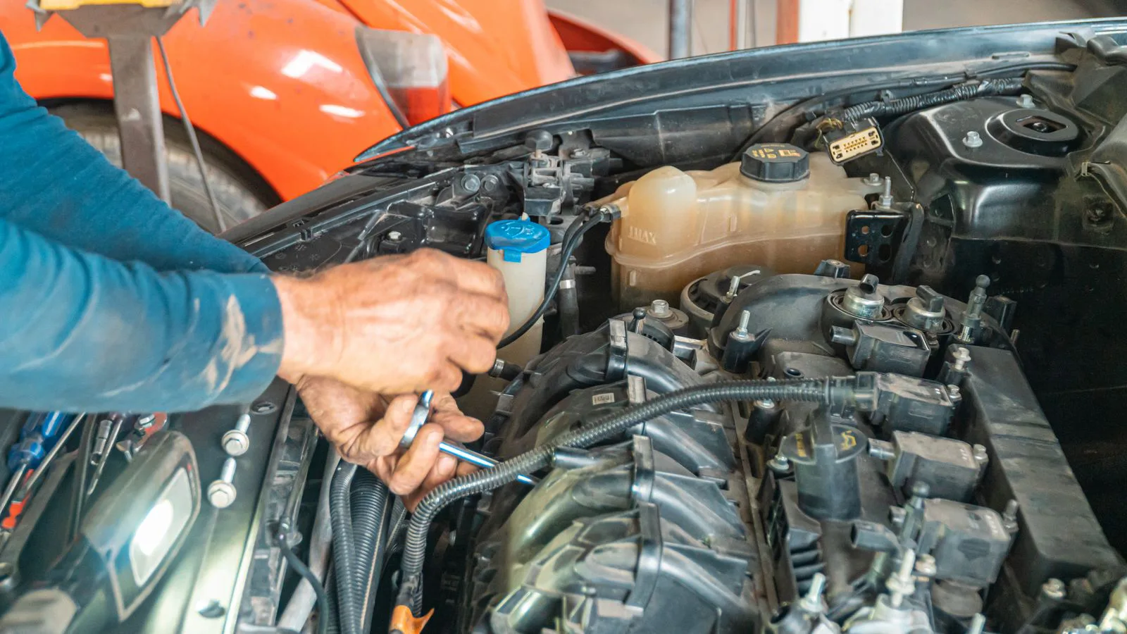 Die Hände eines Mechanikers arbeiten an einer Schraube im Motorraum.