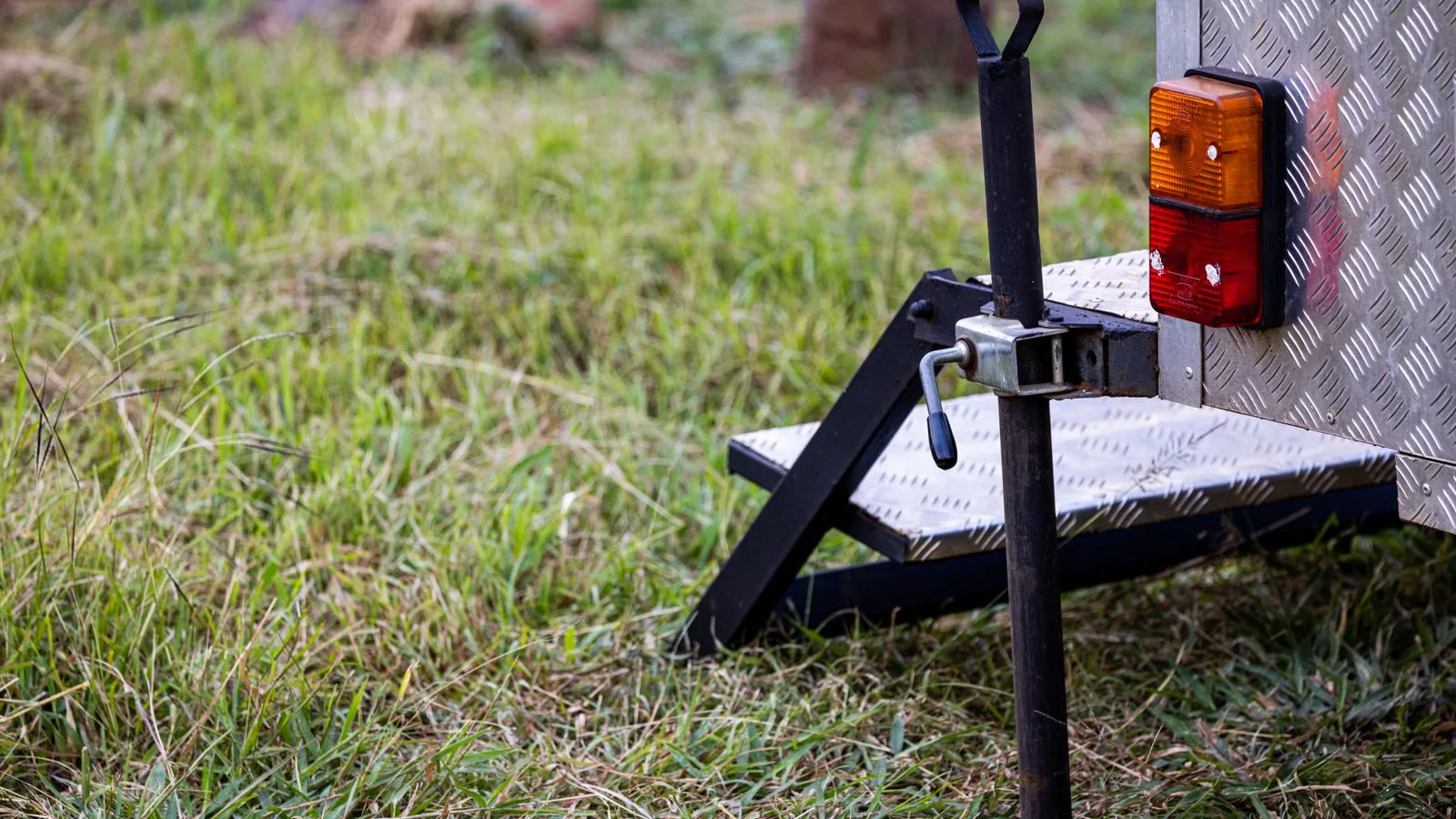 A trailer hitch and jockey wheel resting on grass.