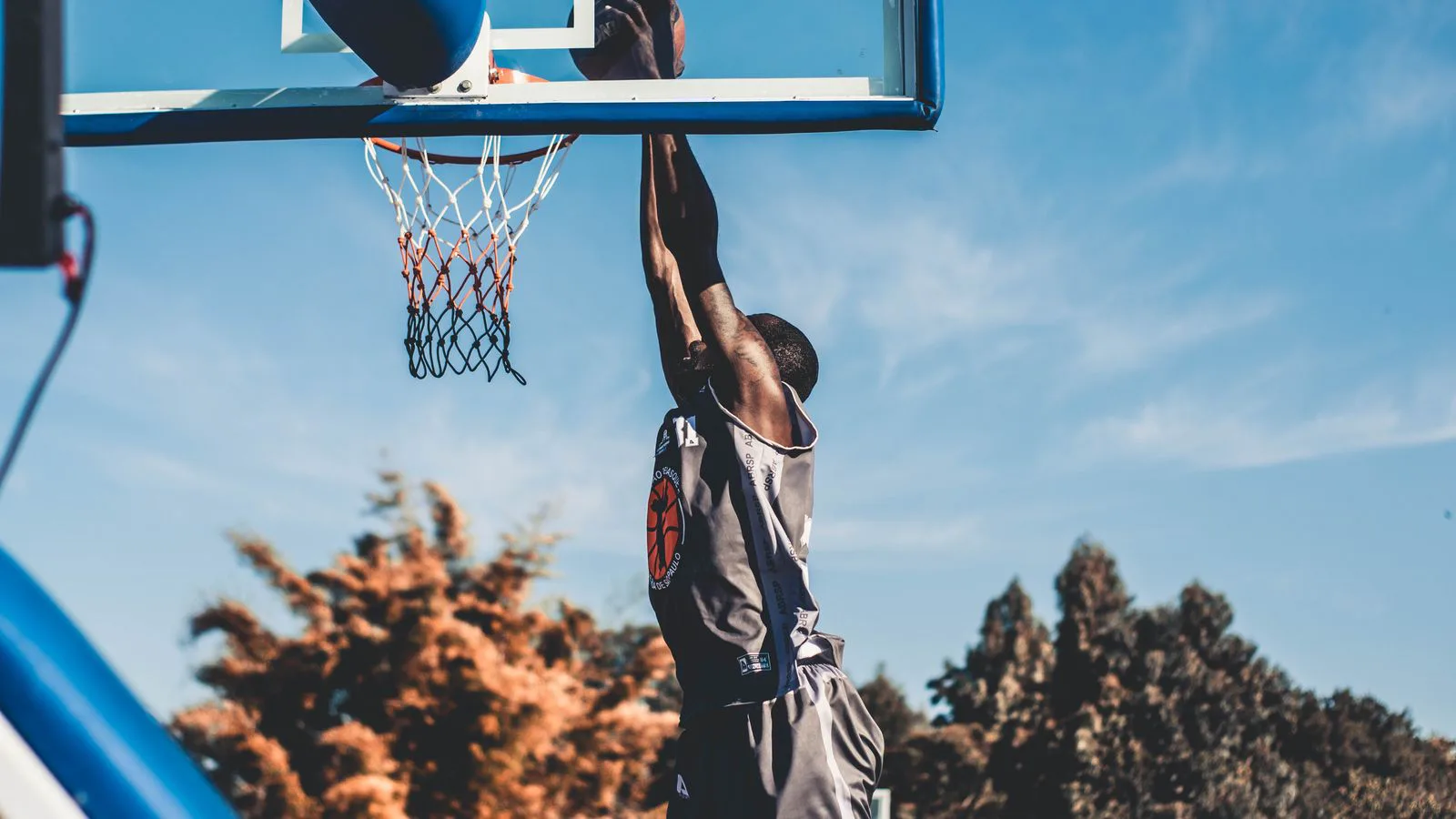 A basketball player rising to dunk on an outdoor court.