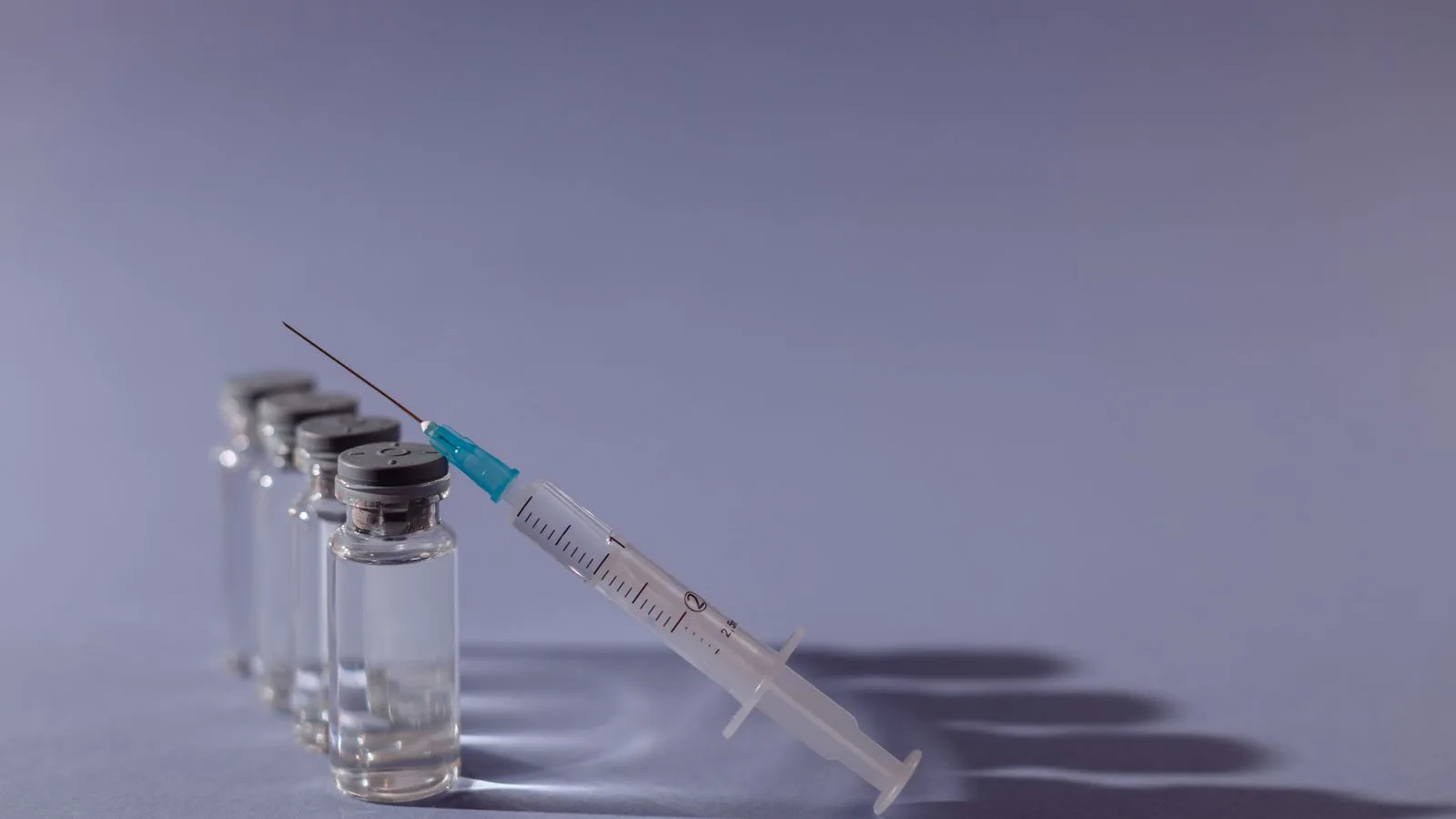 A syringe and glass vials laid out on a grey surface.