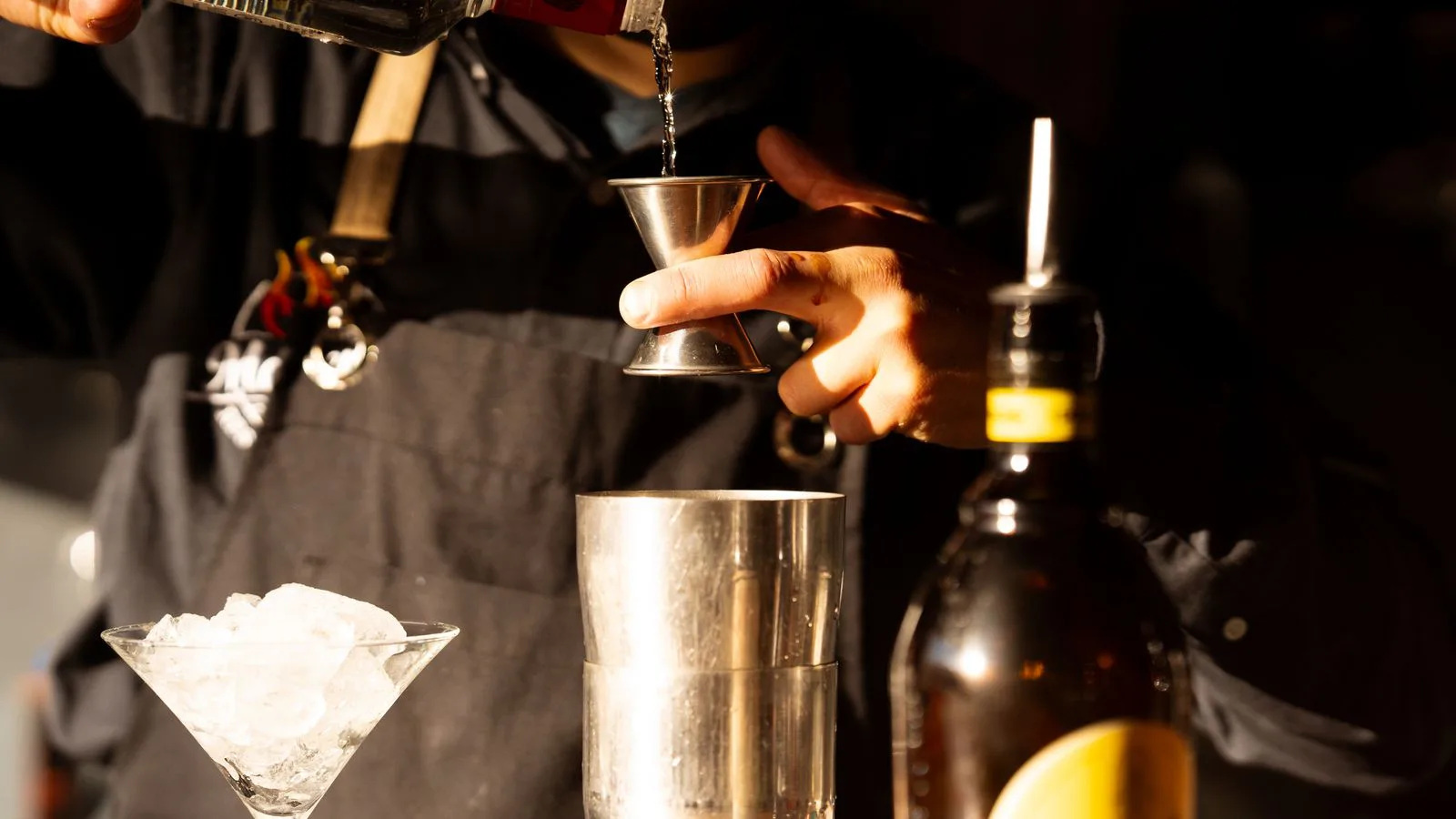 A bartender pouring spirits into a measuring jigger.