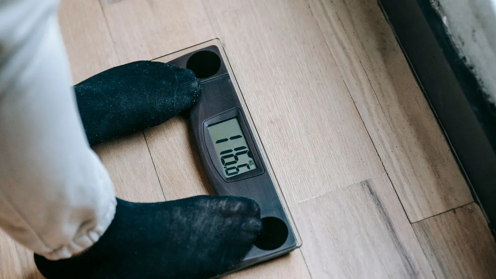 Feet in socks standing on a digital bathroom scale, seen from above.