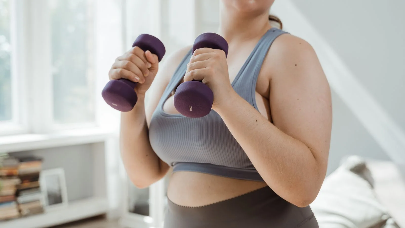 A woman in activewear training with dumbbells indoors.