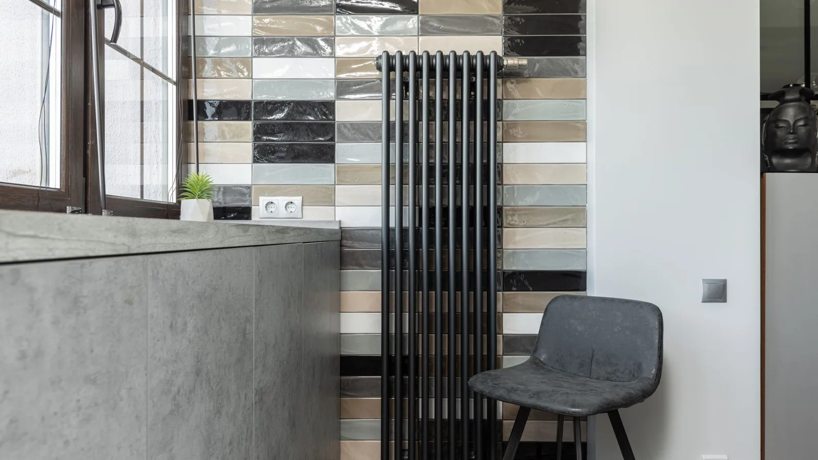 A slim column radiator against a tiled wall in a living room.