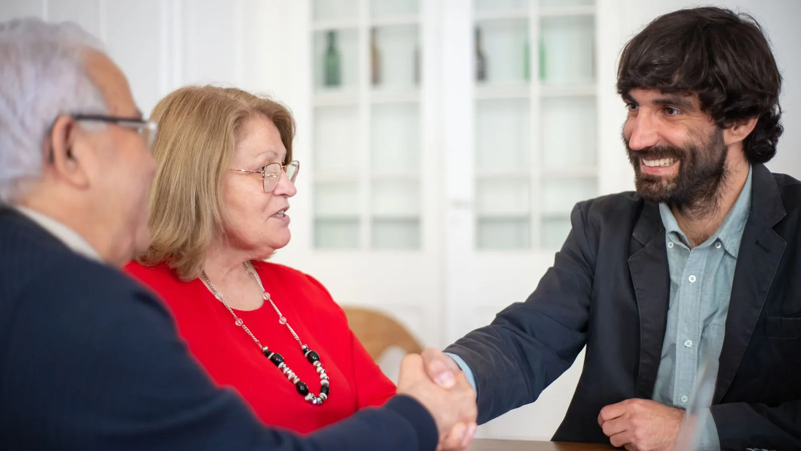 An adviser shaking hands with a couple across an office table.